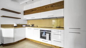 Una cocina moderna con armarios blancos, un panel de madera decorativo, horno empotrado y una encimera con hervidor.