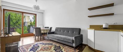A modern living room with a grey sofa, a patterned rug, a wooden cabinet, and a dining area with a table and chairs.