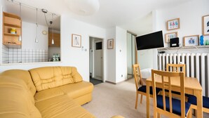 Ein modernes Wohnzimmer mit einem gelben Sofa, einem Esstisch mit Stühlen, einem Flachbildfernseher und gerahmten Bildern an der Wand.