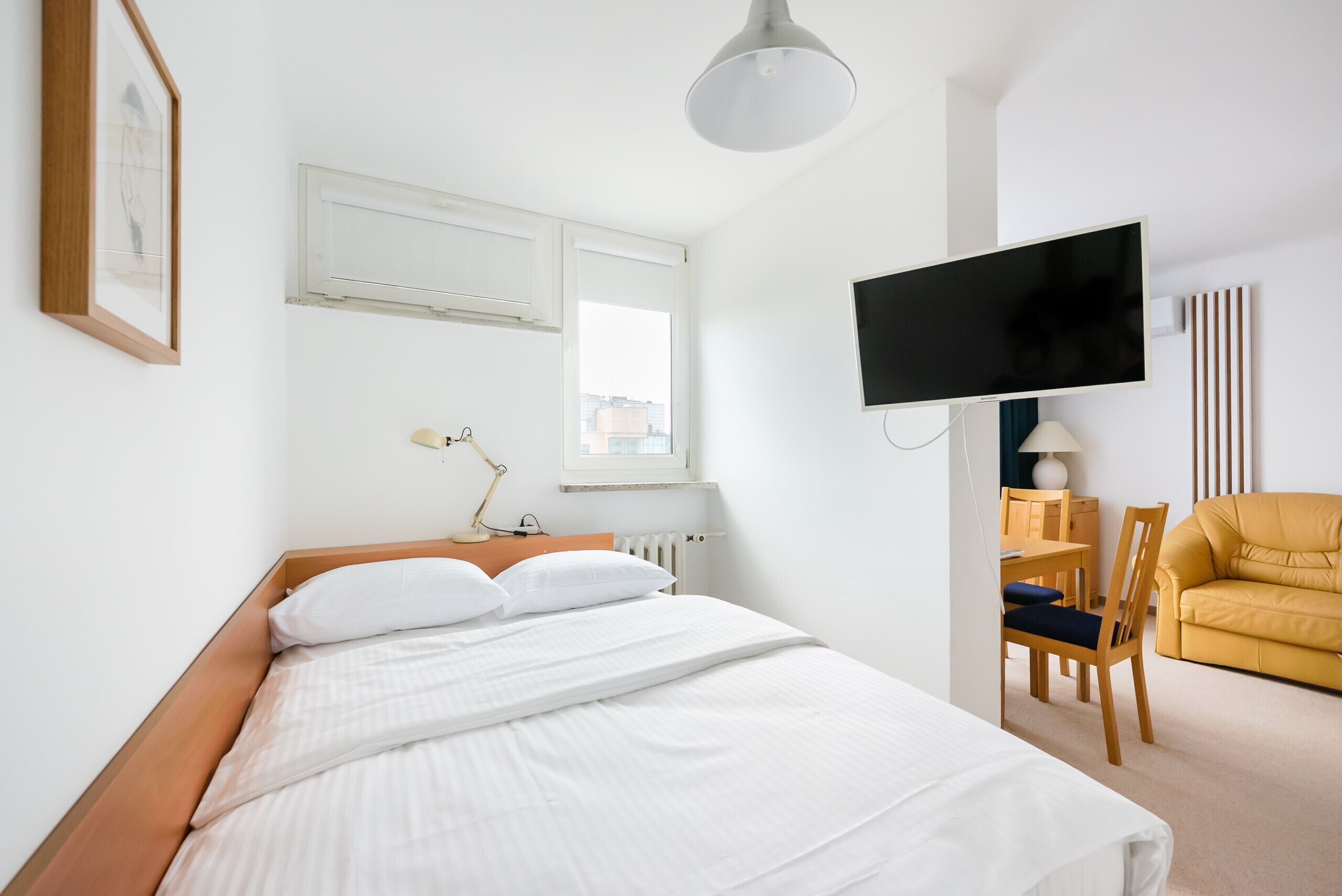 Ein Hotelzimmer mit einem Bett, einem Schreibtisch mit Stuhl, einem an der Wand befestigten Fernseher und einem Fenster.