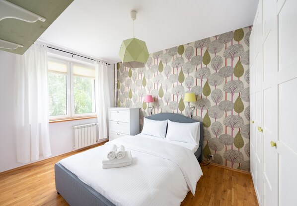 A neatly arranged bedroom with a bed, bedside lamps, a dresser, and a window with curtains.