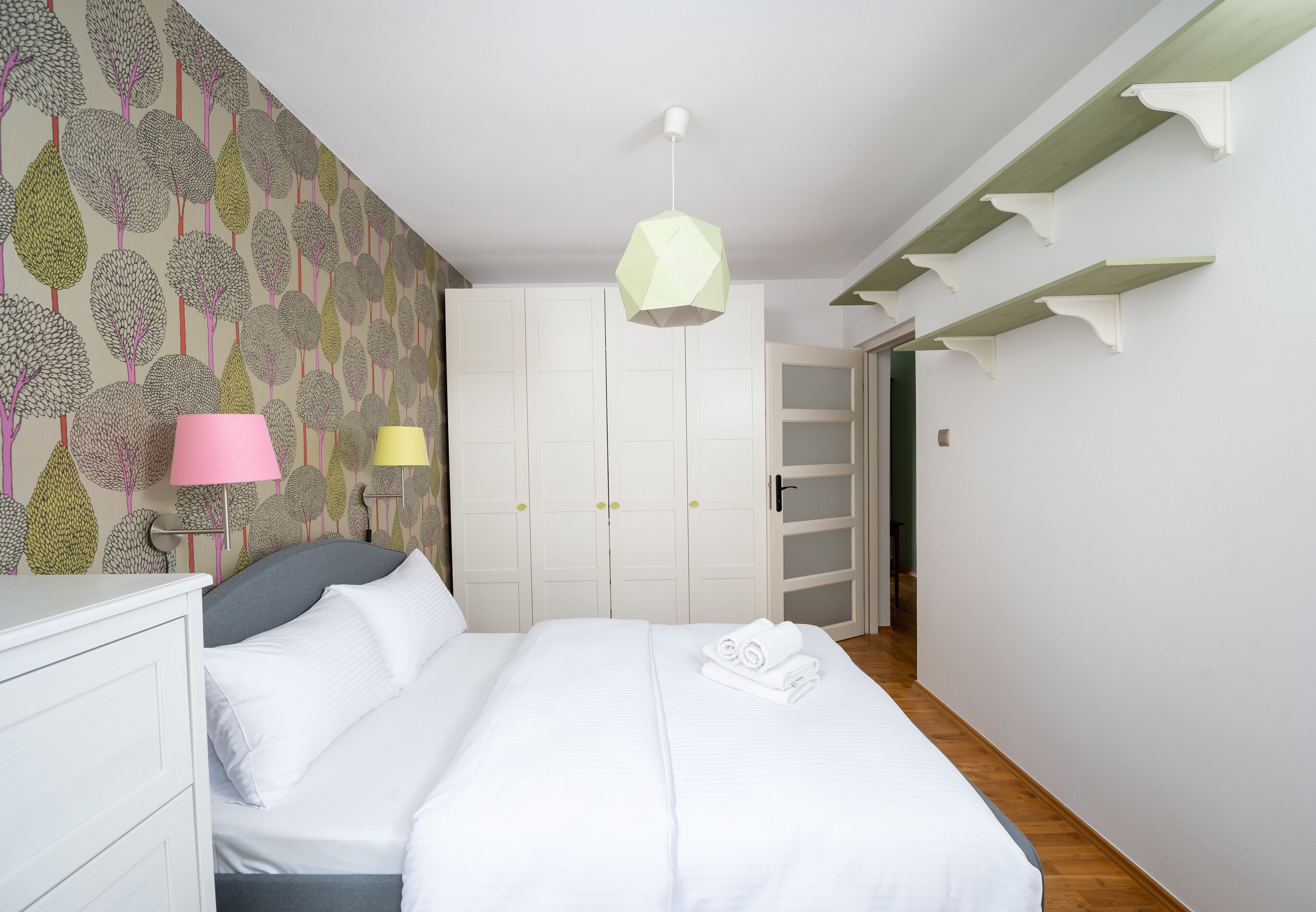A bedroom with a bed, white wardrobe, and a door leading to another room.