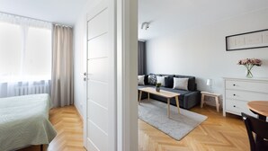 Ein moderner, hell erleuchteter Raum mit einem Bett, einem Schlafsofa, einem kleinen Tisch und einer Kommode.