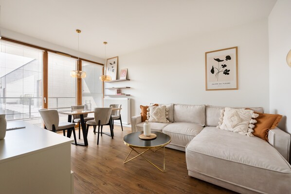 A modern living room with a sofa, dining table, chairs, and artwork on the walls. - Wola Kasprzaka Luxury Apartment (Warszawa)