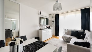 A modern living room with a sofa, a dining table with a cake, and a kitchen area with a TV and cabinets.