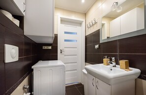 Un baño moderno con inodoro blanco, lavabo con espejo arriba y paredes cubiertas de baldosas marrón oscuro.