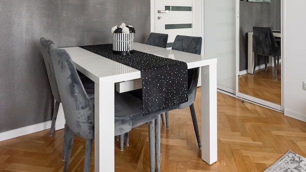 A modern dining area with a white table, grey upholstered chairs, and a chandelier.