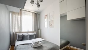 A modern bedroom with a bed, a bedside table, a radiator, and a window with curtains.