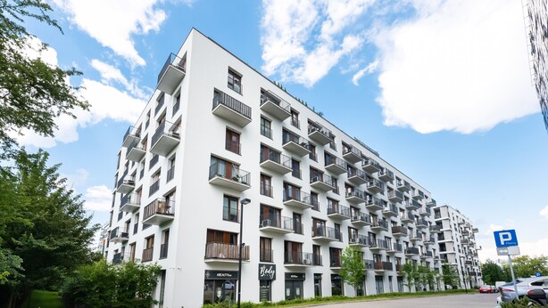 A multi-story residential building with balconies, a parking sign, and a landscaped area with trees and shrubs. - Magazynowa Classy Apartment (Warszawa)