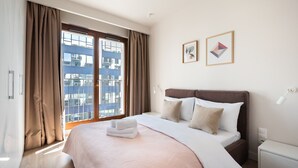 A hotel room with a large bed, a nightstand, a bedside table, and a window with curtains. - Magazynowa Classy Apartment (Warszawa)