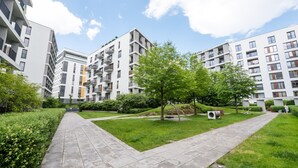 A modern apartment complex with multiple buildings, a central grassy area with trees, and a paved walkway. - Magazynowa Classy Apartment (Warszawa)