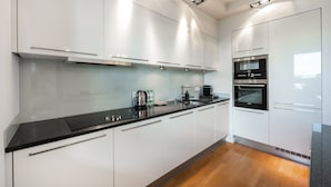 A modern kitchen with white cabinets, black countertops, stainless steel appliances, and under-cabinet lighting. - Mokotów Serenity Premium Apartment (Warszawa)
