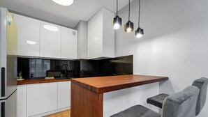 Eine moderne Küche mit weißen Schränken, einer Holz Arbeitsplatte und einem schwarzen Herd. Drei Pendelleuchten hängen über der Arbeitsfläche.