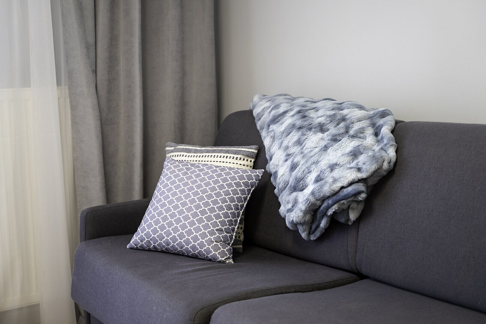 Un sofá gris con un cojín estampado y una manta mullida de color gris.