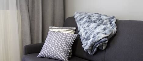 Un sofá gris con un cojín estampado y una manta mullida de color gris.