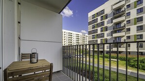 Ein Balkon mit Holztisch und Stuhl, einer Metalllaterne und Blick auf ein mehrstöckiges Wohngebäude mit Balkonen.