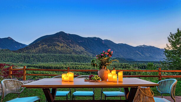 An outdoor dining table with candles, chairs, and a hat on the table.