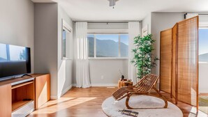 A modern living room with a flat-screen TV, wooden flooring, a large window with mountain views, a bamboo plant, and a traditional sliding door.