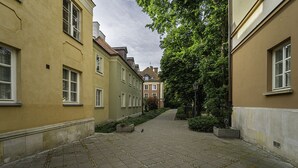Une ruelle étroite pavée, bordée de bâtiments historiques aux fenêtres uniformes et traversée par un chemin central bordé d’arbres.