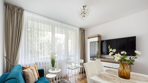 Una sala moderna con un sofá azul, una mesa de comedor con un jarrón de flores y un televisor de pantalla plana grande.