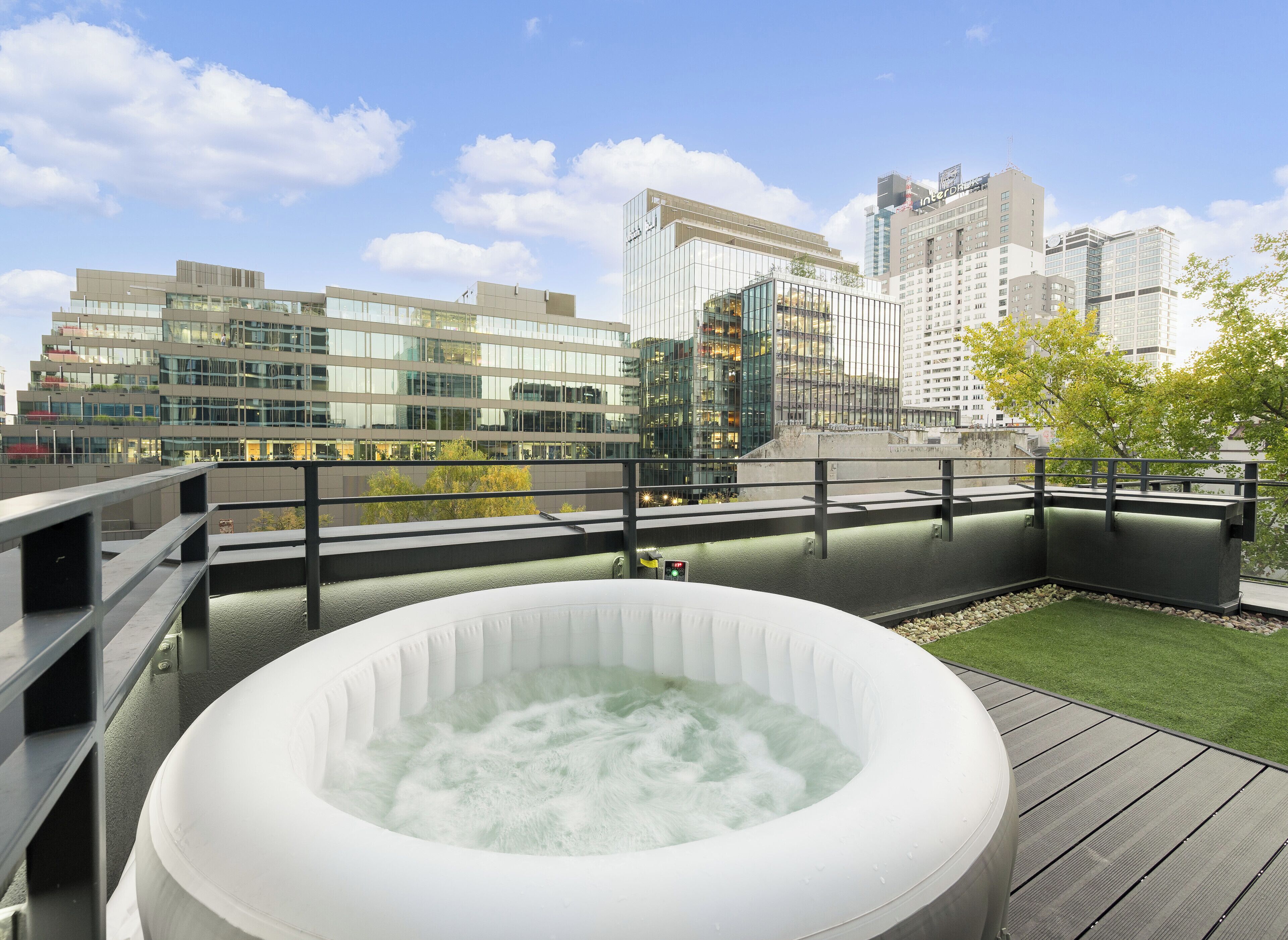 Une terrasse sur le toit avec un jacuzzi, une terrasse en bois et une vue sur des immeubles modernes.