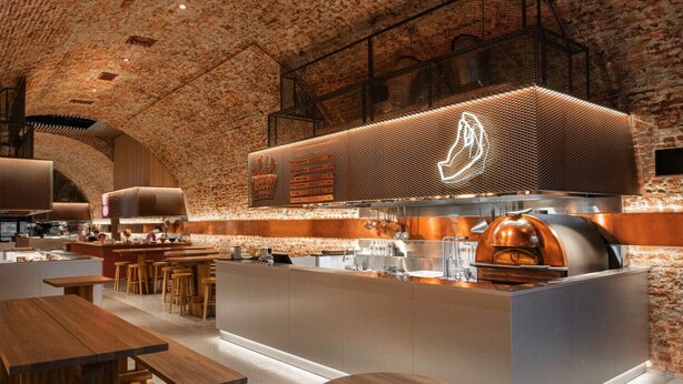 A modern kitchen with a brick wall, wooden bar stools, and a neon sign.