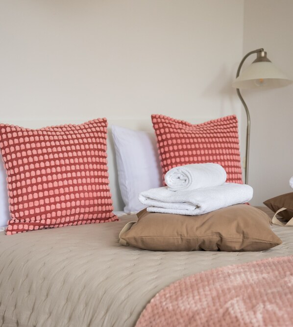 A neatly made bed with red and white patterned pillows, a folded white towel, and a brown pillow.