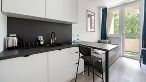 A modern kitchen with a black countertop, white cabinets, and a built-in stove. There is a window with blue curtains and a view of greenery outside.