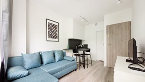 A modern living room with a blue sofa, a dining area with a black table and chairs, and a TV on a white stand.