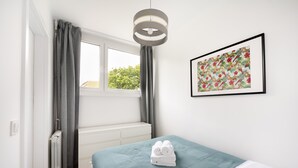 Et soveværelse med en seng, en radiator, et vindue med gardiner, et billede hængt på væggen og en loftslampe.