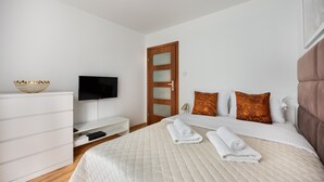A modern bedroom with a bed, a TV, a dresser, and a wooden door.