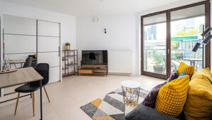 A modern living room with a dining area, a TV, and a large window with a view of buildings.