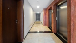 A hallway with wooden doors, elevators, and a tiled floor.