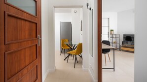 A modern interior with a wooden door, a dining area with yellow chairs, and a TV in the background.