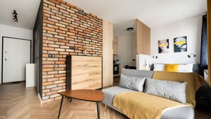 A modern living room with a brick accent wall, a wooden herringbone floor, a sofa with a mustard throw, and a small wooden table. - Woronicza 80 Modern Studio (Warszawa)