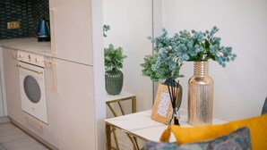 Moderni keittiö, jossa on valkoinen työtaso, kultaisella kehyksellä varustettu pöytä ja koristeellisia kasveja.
