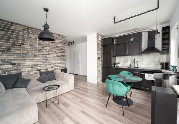 Relax in this stylish living space featuring a brick accent wall, neutral-toned sofa, and compact kitchen area.