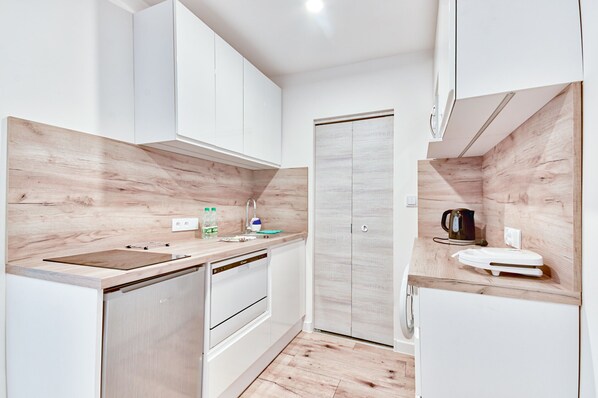 A compact kitchen with white cabinetry, a wooden countertop, a dishwasher, a microwave, and a kettle.