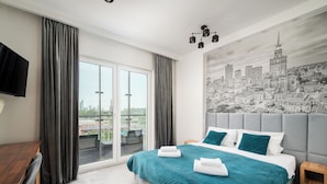Quarto de hotel moderno com cama grande, cabeceira cinza, roupa de cama verde-água e um mural com vista para a cidade na parede.