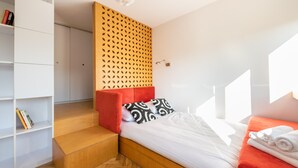 A modern bedroom with a wooden headboard, a red accent pillow, a white bedspread, and a neatly made bed. - Spiska Standard Studio (Warszawa)