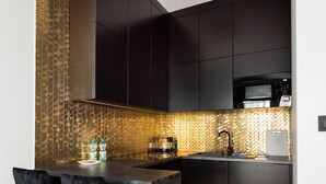 A modern kitchen with dark cabinetry, a black countertop, and a herringbone-patterned backsplash. - Varsovia Comfort 204 (Warszawa)