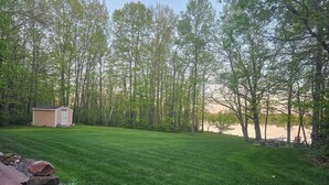 Une pelouse bien entretenue, un petit abri de jardin et un lac avec des arbres en arrière-plan.