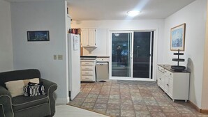 Un espace de vie compact comprenant un canapé, une kitchenette et une porte-fenêtre coulissante donnant sur une terrasse.
