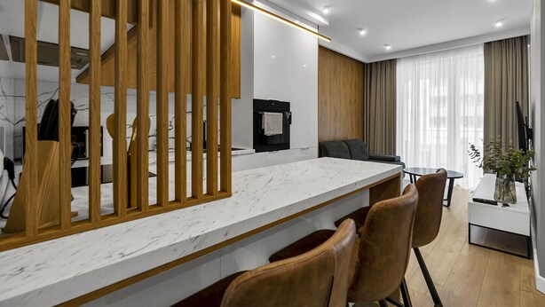 A modern kitchen with a marble countertop, wooden panel divider, and a dining area with a table and chairs. - Lotnisko Chopina Modern Apartment (Warszawa)