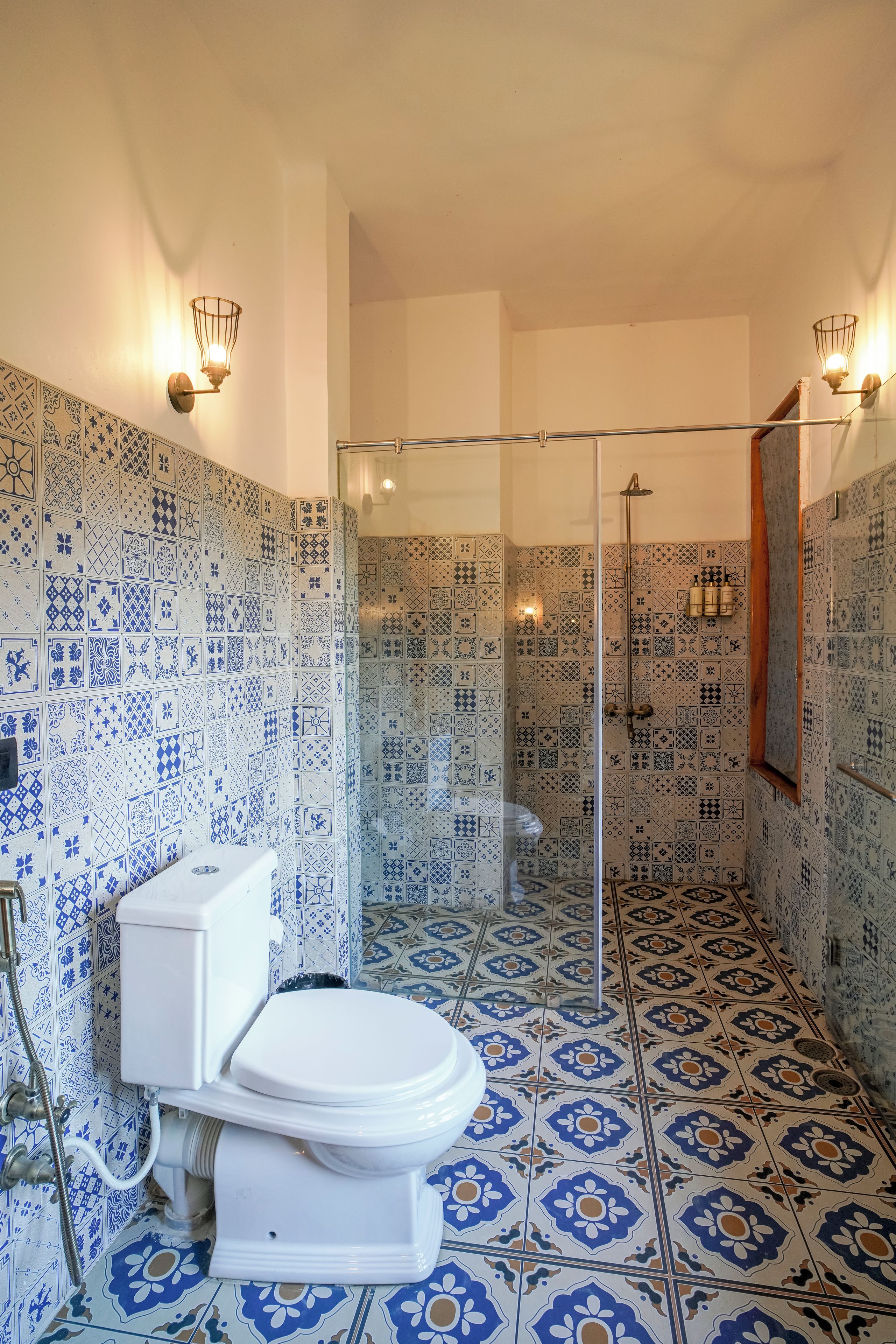 Un baño con inodoro blanco, cabina de ducha de vidrio y baldosas estampadas en paredes y suelo.