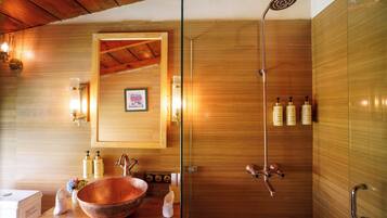 A bathroom with a wooden interior, a large copper basin, a shower with a rain showerhead, and toiletries on the counter.