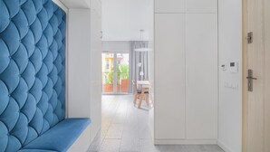A hallway with a blue upholstered bench, a white wardrobe, and a door with a wooden frame. - Warta River Comfort Apartment (Poznań)