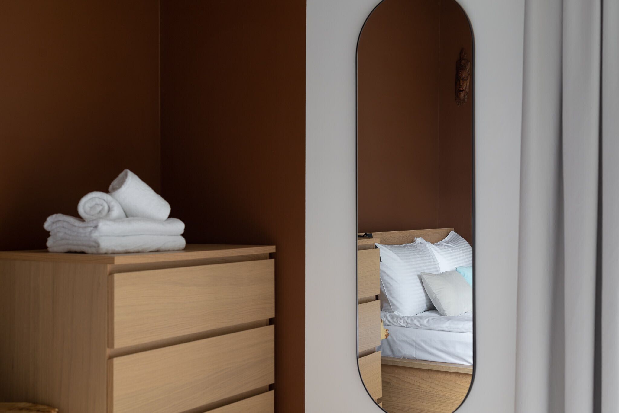 Habitació d'hotel amb un taulell de fusta, un mirall que reflecteix un llit amb roba de llit blanca i una tovallola ben arrugada damunt del taulell.