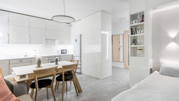 A modern kitchen with white cabinets, a dining table, and chairs. There is a refrigerator, a microwave, and a coffee machine on the counter. - Warta River Comfort Apartment (Poznań)