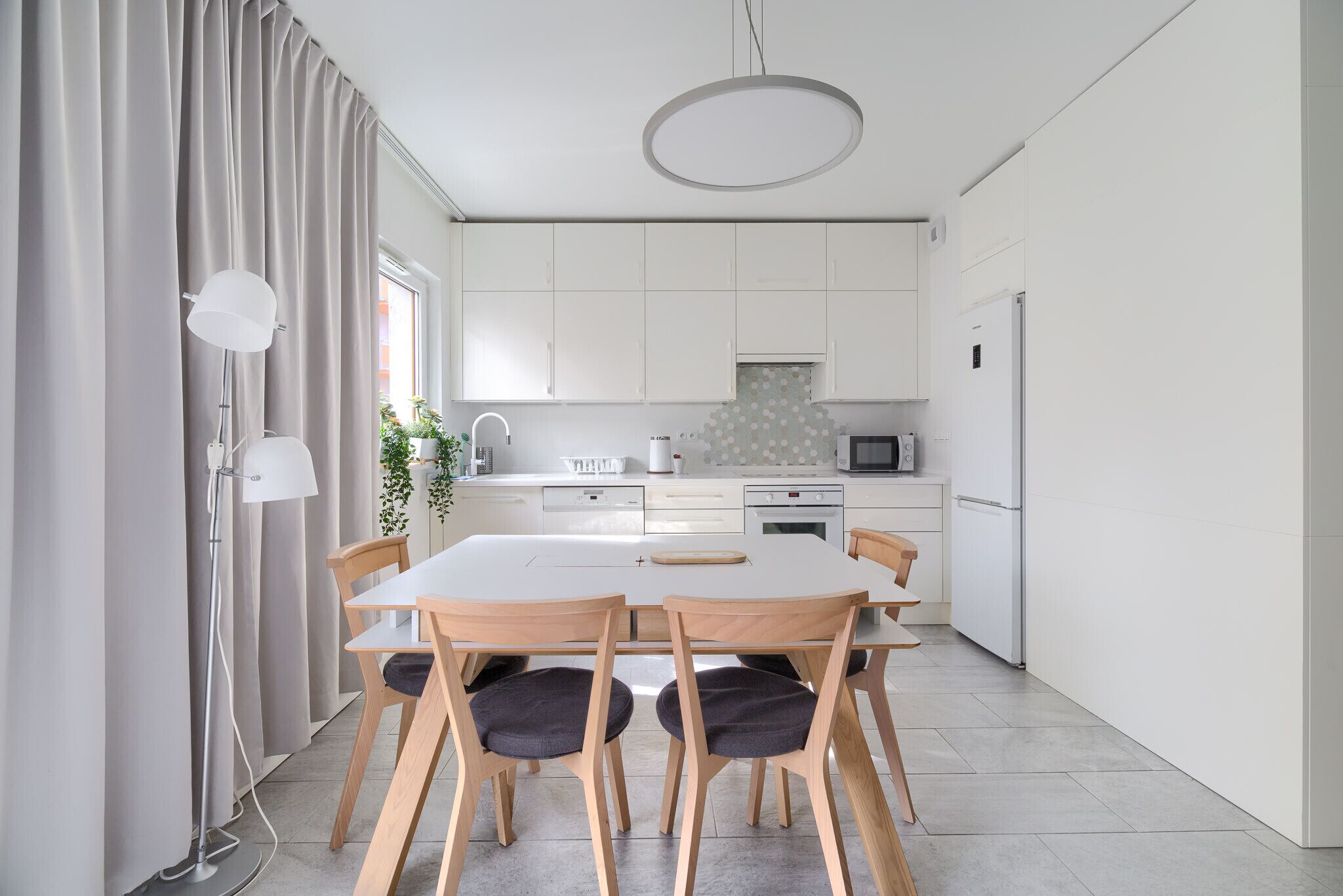A modern kitchen with white cabinets, a central island, and a dining area with a table and chairs.